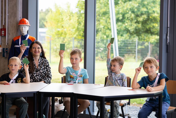 Das Bild zeigt die Kinder und Erzieherin des Kinderland Pausa. Sie halten gr&uuml;ne Karten hoch.